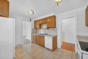 Kitchen with white appliances, light tile patterned flooring, light countertops, and wood finish cabinetry