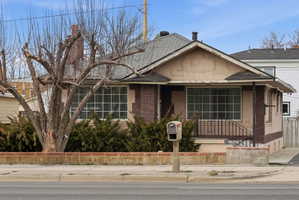View of front of home with a shingled roof, brick siding, a porch, and stucco siding