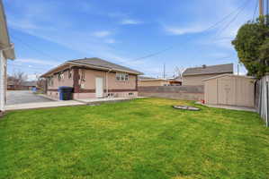 Back of house with a fenced backyard, a patio, a storage unit, and an outdoor fire pit