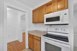 Kitchen featuring white appliances, light countertops, wood finish cabinets, and light wood-style floors