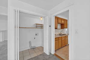 Laundry area with light tile patterned floors, hookup for a washing machine, electric dryer hookup, and light carpet
