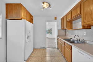 Kitchen featuring white appliances, light countertops, wood finish cabinets, light tile patterned floors, and a textured ceiling