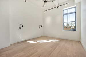 Spare room with rail lighting, a ceiling fan, light wood-type flooring, and a high ceiling