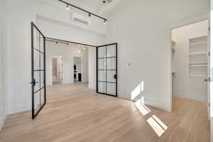 Unfurnished bedroom with a walk in closet, light wood-style flooring, french doors, and track lighting