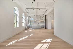 Unfurnished living room featuring a high ceiling, light wood-style flooring, and rail lighting