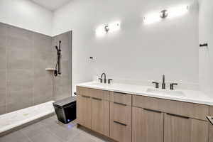 Full bath featuring double vanity, light tile patterned floors, and a tile shower