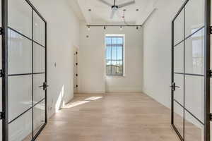 Spare room with french doors, light wood-style flooring, ceiling fan, and a high ceiling