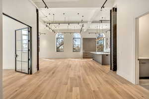 Unfurnished dining area featuring light wood-style floors, rail lighting, and beamed ceiling