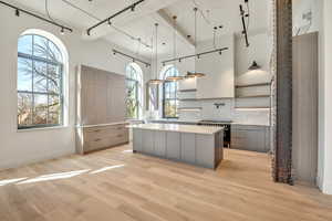 Two tone kitchen with open shelves, modern cabinets, tasteful backsplash, a center island, and a high ceiling