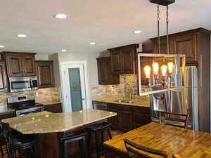 Kitchen with dark wood finish cabinets, stainless steel appliances, light stone counters, and a breakfast bar