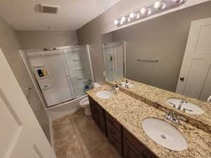 Full bathroom with double vanity, combined bath / shower with glass door, and a textured ceiling