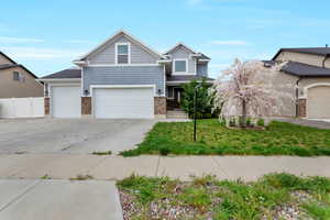 Craftsman-style home featuring concrete driveway, a garage, stone siding, a front lawn, and a gate