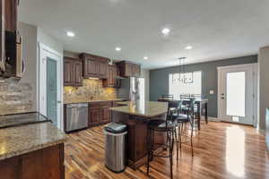 Kitchen featuring light stone counters, a kitchen bar, dark wood finish cabinetry, a kitchen island, and backsplash