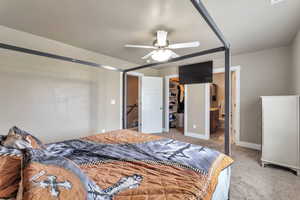 Bedroom with ensuite bathroom, light carpet, a ceiling fan, and a walk in closet