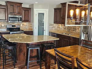 Kitchen with stainless steel appliances, dark wood finish cabinets, light stone counters, tasteful backsplash, and dark wood-style floors