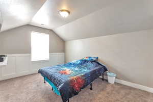 Bedroom with carpet, a textured ceiling, a decorative wall, and wainscoting