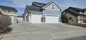 View of front of home with solar panels, concrete driveway, stone siding, roof with shingles, and an attached garage