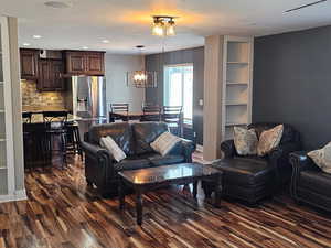 Living room with built in shelves, dark wood-type flooring, and hanging lights