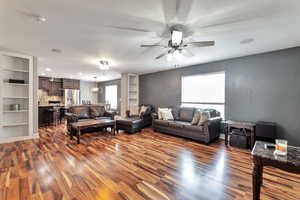 Living room featuring built in shelves, dark wood-type flooring, a chandelier, and ceiling fan