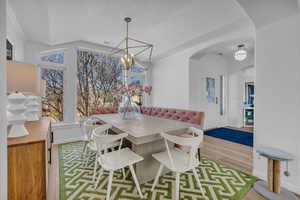 Dining room featuring vaulted ceiling, light wood-style floors, arched walkways, and hanging lights