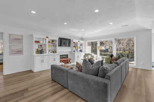 Living room featuring light wood-style floors, ornamental molding, a glass covered fireplace, and recessed lighting