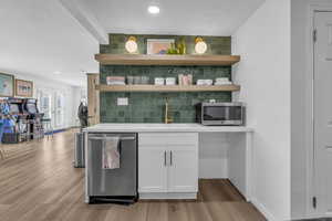 Bar featuring tasteful backsplash, stainless steel appliances, white cabinets, light wood-style floors, and french doors