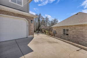 View of home's exterior with brick siding, a patio area, roof with shingles, driveway, and a garage