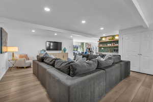 Living room with light wood-style floors, recessed lighting, bar area, and beam ceiling