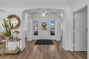 Entrance foyer featuring arched walkways, light wood-style floors, and crown molding