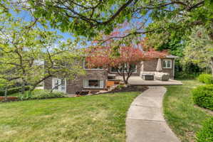 Brick exterior with a concrete patio, curved walkway, mature trees, and tiered landscaping