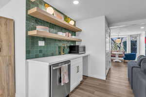 Kitchen featuring stainless steel appliances, white cabinets, tasteful backsplash, open floor plan, and light wood-type flooring