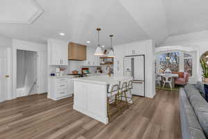Kitchen with open floor plan, dark wood finished floors, high end fridge, an island with sink, and a kitchen bar