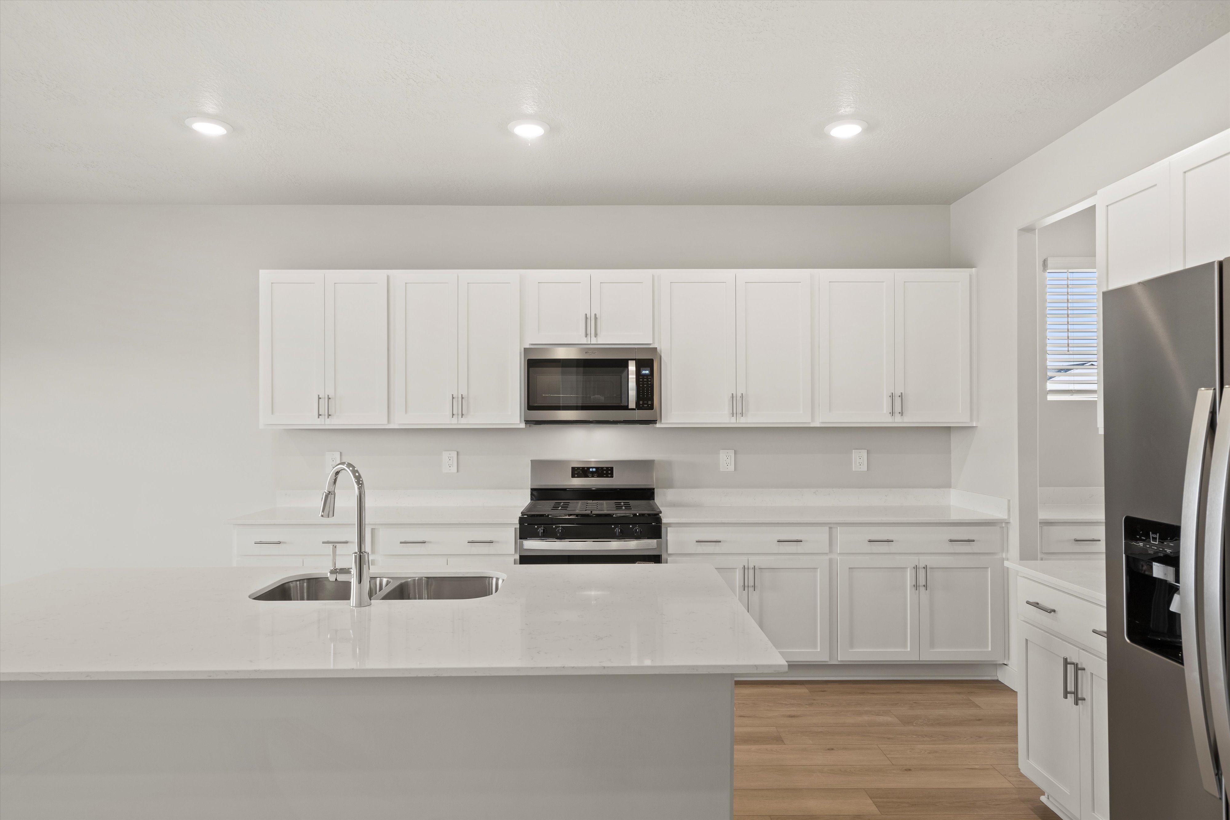 Kitchen featuring stainless steel appliances, light wood finished floors, white cabinetry, light stone counters, and recessed lighting
