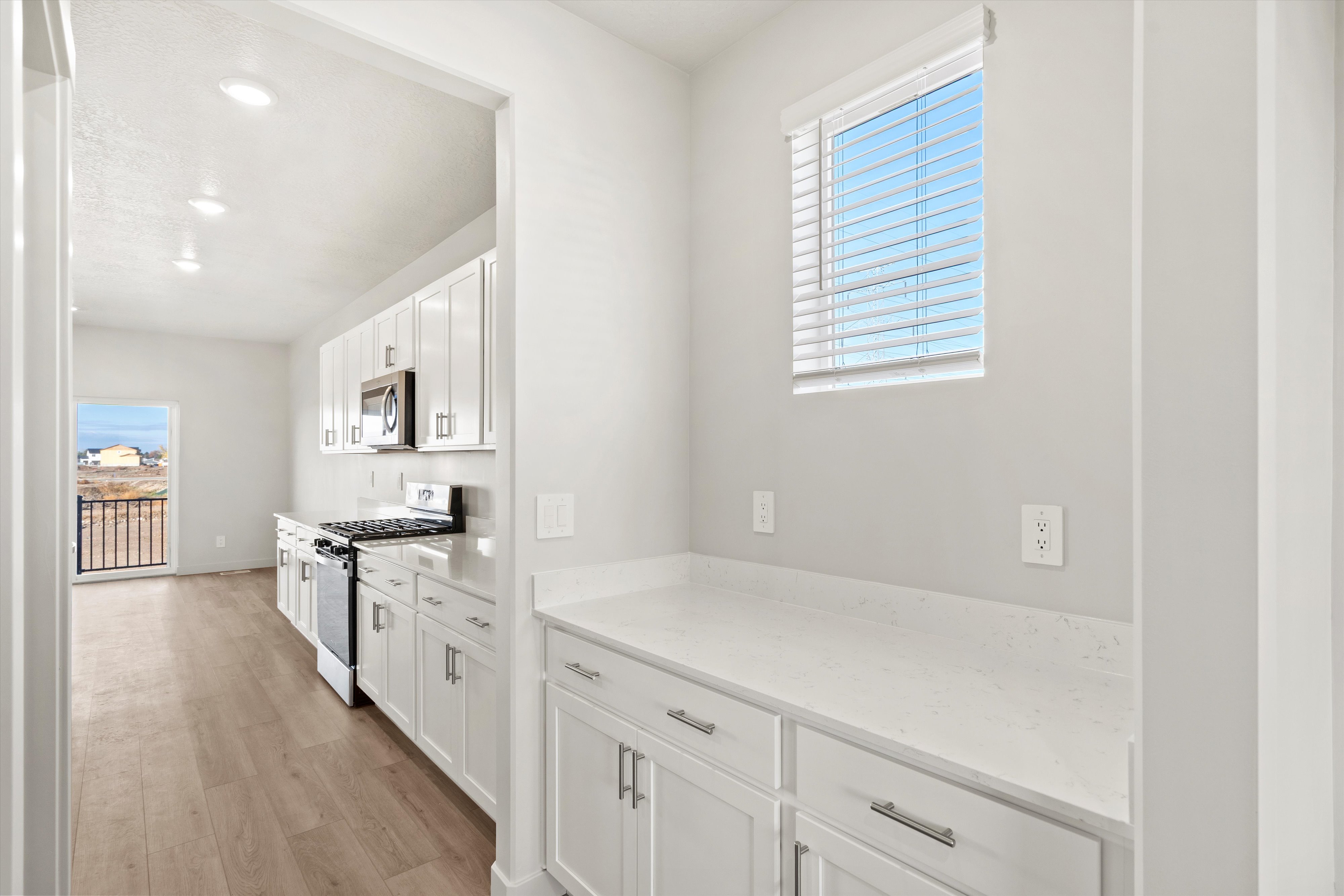 Kitchen featuring stainless steel appliances, white cabinetry, light wood finished floors, recessed lighting, and light stone countertops