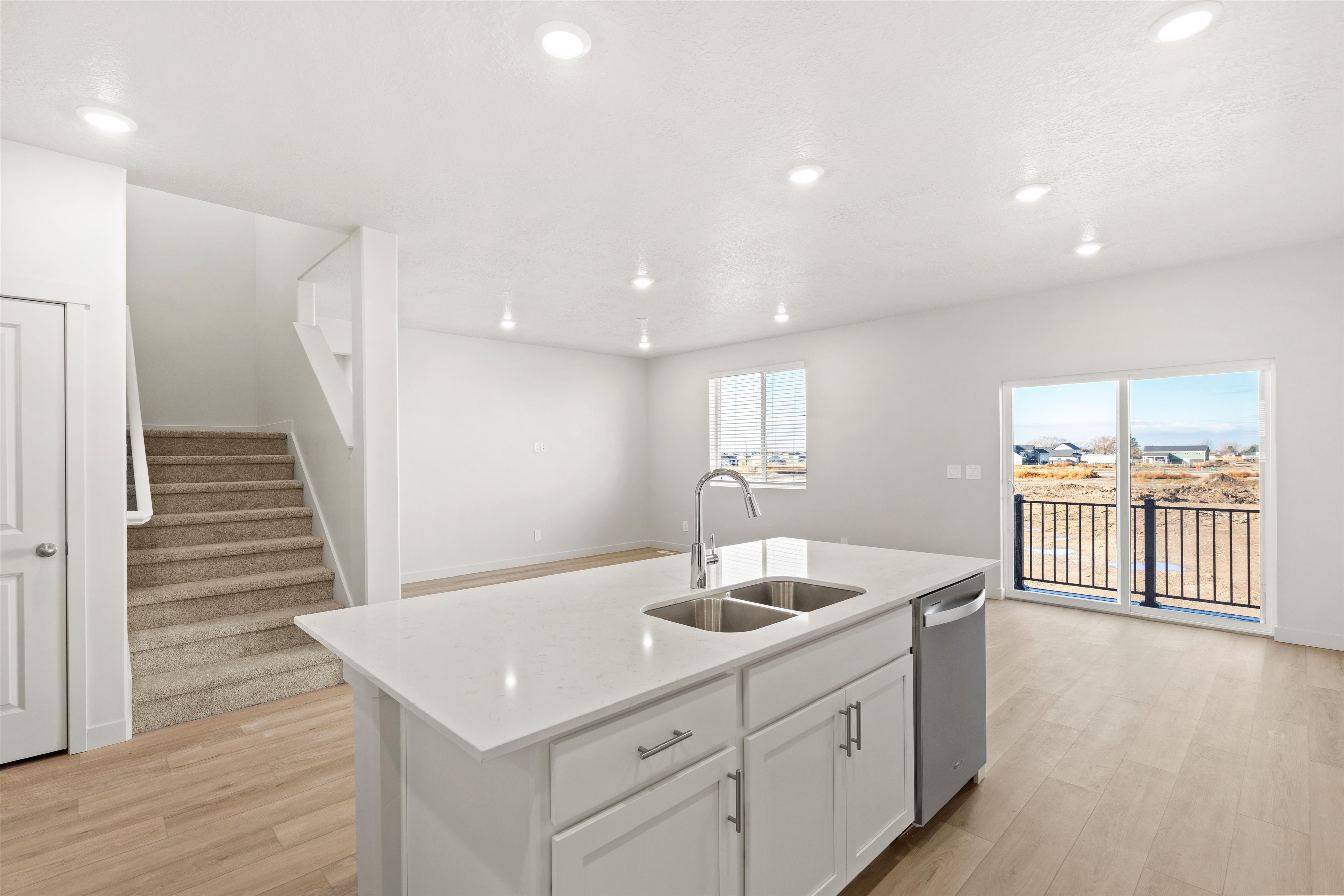 Kitchen featuring light wood finished floors, white cabinetry, a center island with sink, light stone countertops, and dishwasher