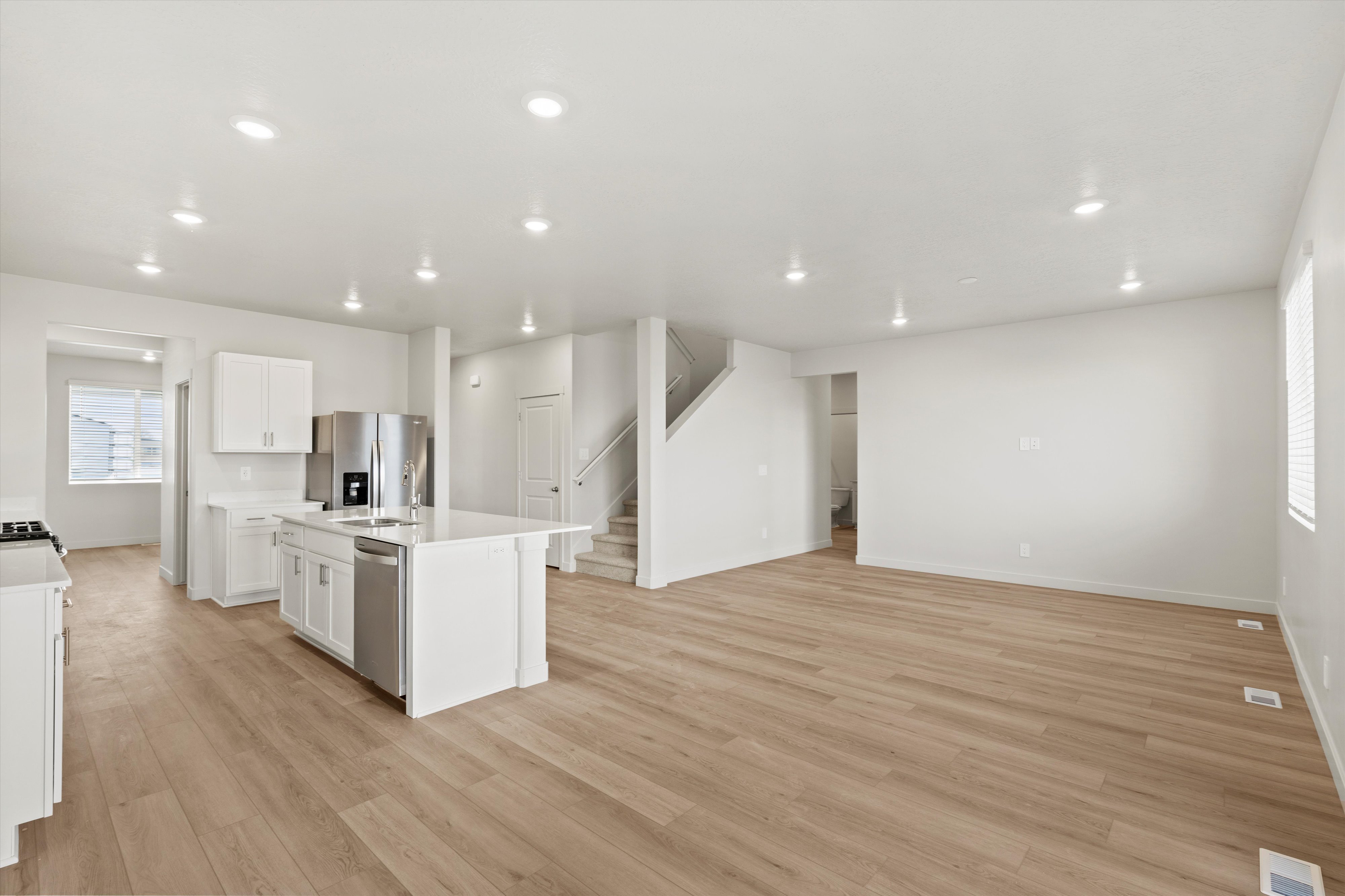 Kitchen with an island with sink, light wood-style floors, open floor plan, stainless steel appliances, and white cabinets