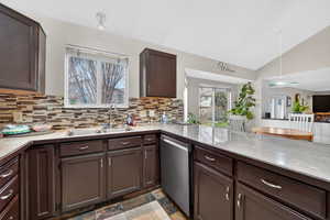 Kitchen featuring dark wood finish cabinets, stainless steel dishwasher, lofted ceiling, light countertops, and light stone finish flooring