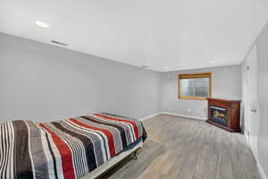 Bedroom featuring a lit fireplace, light wood-style floors, and recessed lighting