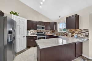 Kitchen with stainless steel appliances, dark wood finish cabinetry, a peninsula, light countertops, and vaulted ceiling
