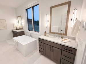 Full bathroom featuring two vanities, a soaking tub, and light marble finish floors