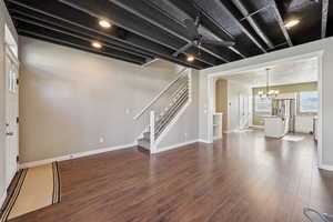 Unfurnished living room featuring exposed rafts, surround sound, ceiling fan, and dark wood like floors.