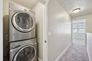 Laundry area with stacked washer and dryer, a textured ceiling, and light colored carpet
