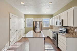 Kitchen featuring stainless steel appliances, light stone countertops, white cabinetry, tasteful backsplash, and recessed lighting