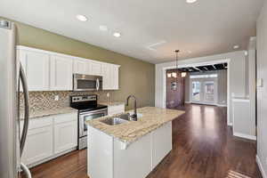Kitchen featuring stainless steel appliances, a center island with sink, light stone countertops, and white cabinets