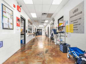 Hallway with a drop ceiling, concrete block wall, and finished concrete floors