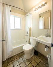 Bathroom with stone tile flooring, a textured wall, and shower / bath combination with curtain