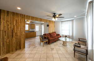 Living room featuring light tile patterned flooring, ceiling fan, wood walls, and recessed lighting
