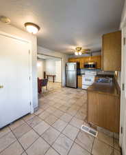Kitchen with stainless steel appliances, dark countertops, wood finish cabinetry, a textured ceiling, and a ceiling fan