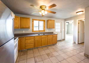 Kitchen featuring freestanding refrigerator, ceiling fan, dark countertops, white range with electric cooktop, and a textured ceiling