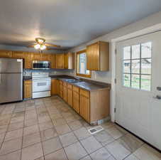 Kitchen with stainless steel appliances, wood finish cabinets, dark countertops, and light tile patterned floors